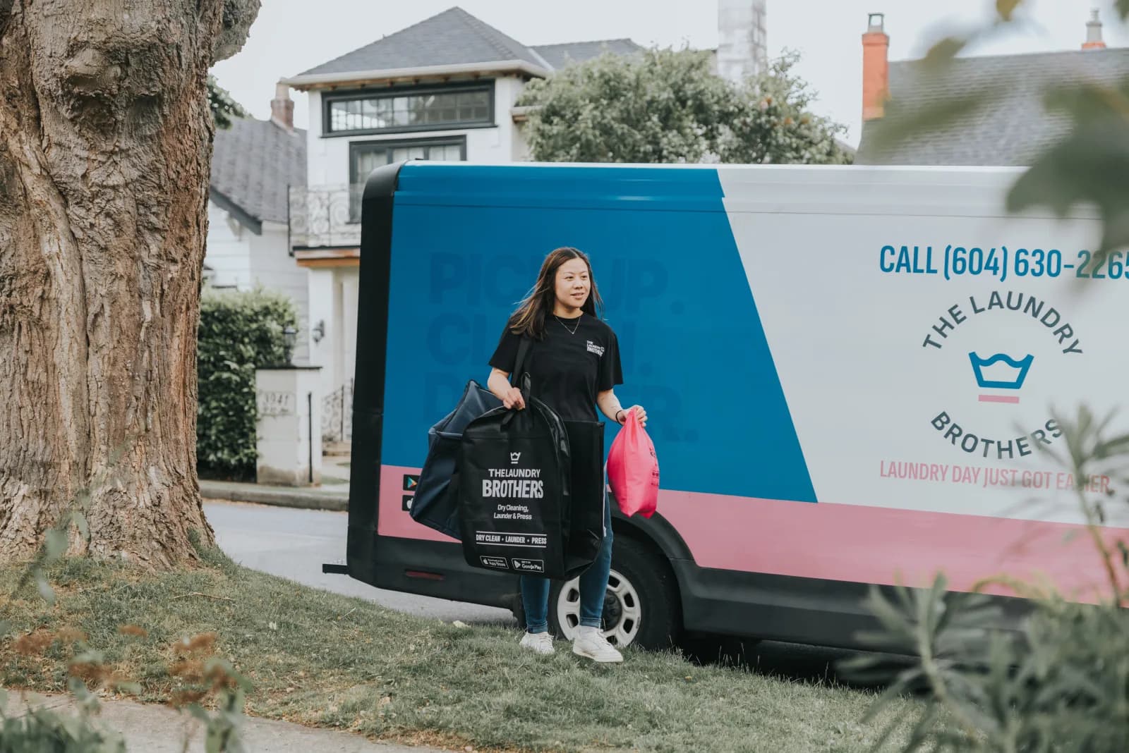 A Laundry Brothers driver leaning against the branded delivery van on a quiet residential street.