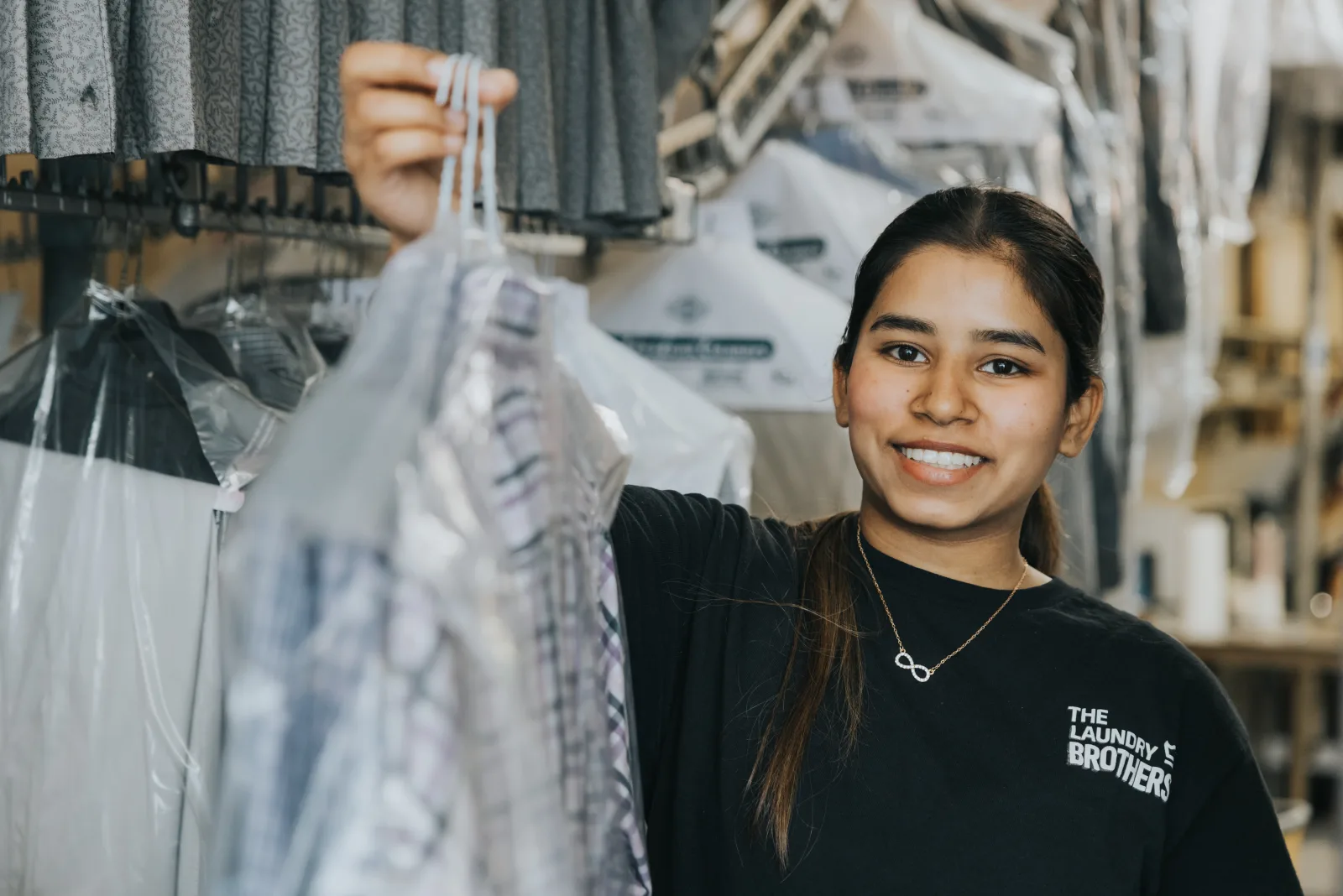A Laundry Brothers team member smiling with a freshly cleaned, pressed garment.