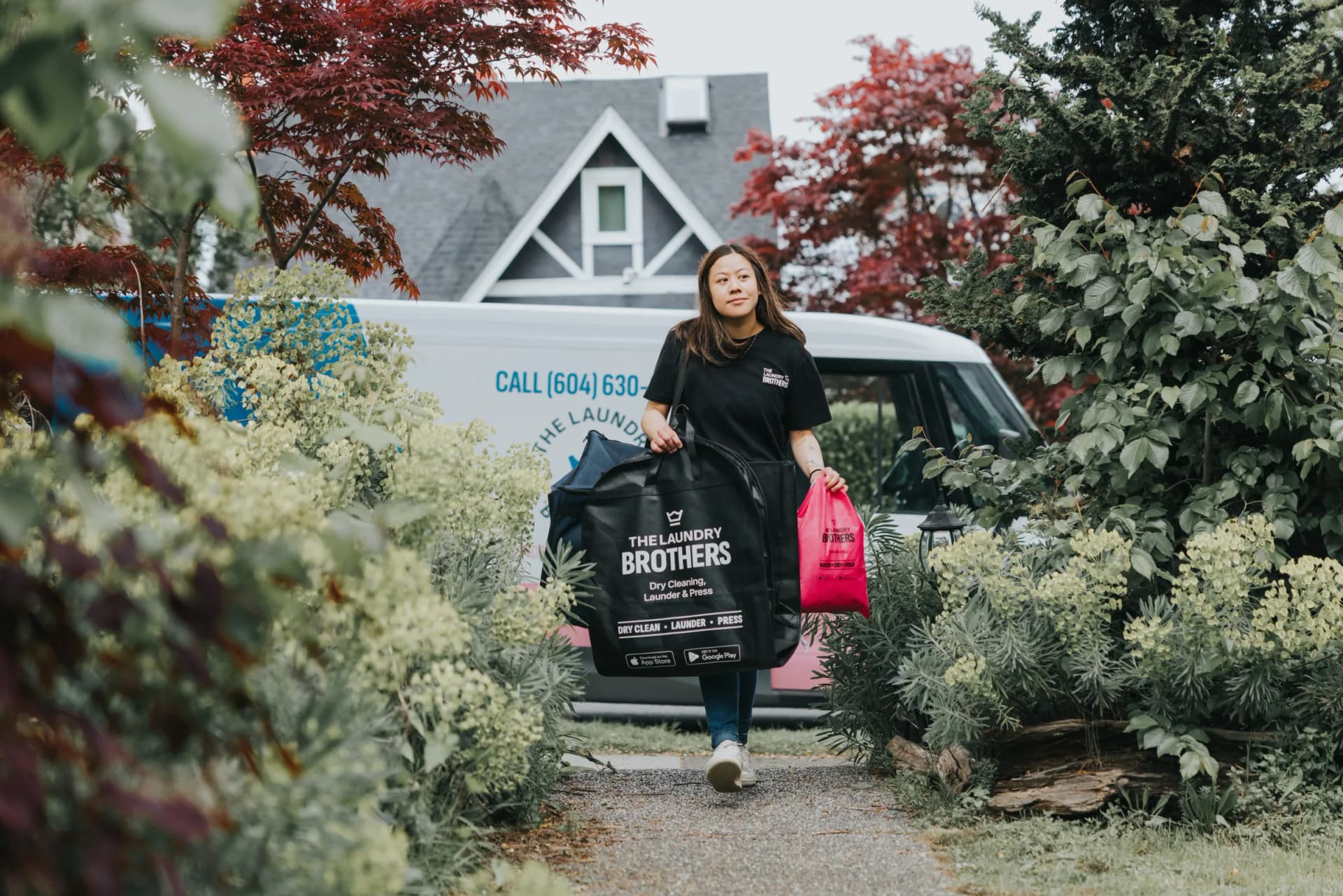 A Laundry Brothers driver walking through a garden path carrying TLB bags, with the branded van in the background.